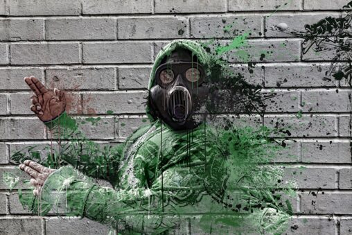 Figure in green wearing gas mask and hood against brick wall