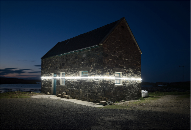stone cottage in near darkness with line of white light projected across it horizontally