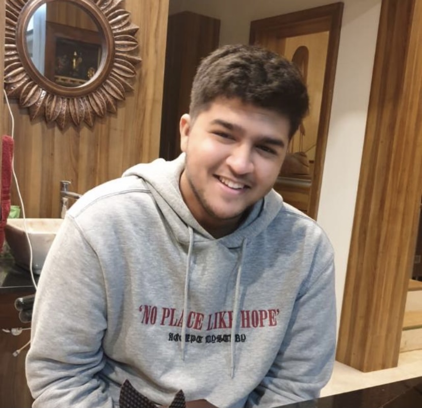 A photograph of Jordyn's friend Siddhant. He has brown hair and is wearing a grey sweatshirt with words "No place like hope". He is smiling, probably caught laughing.