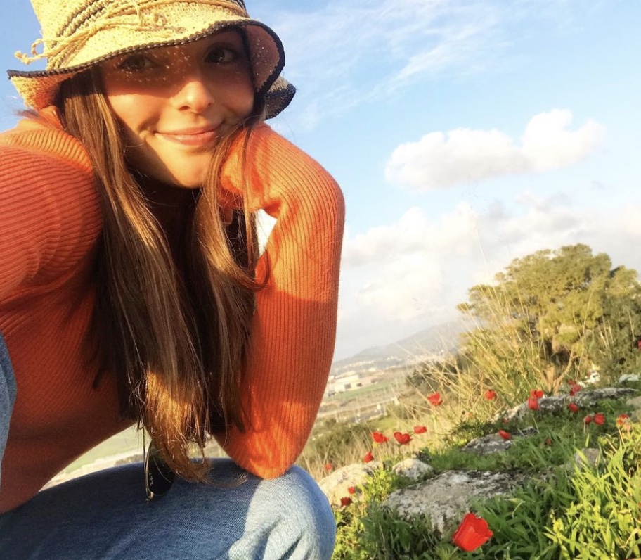 A selfie of Jordyn's friend Alexa. She is wearing a bucket hat, and her red shirt matches the red poppies around her. She is smiling. 
