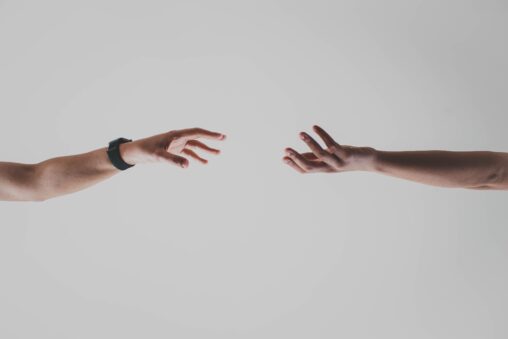 A picture of two hands reaching towards each other. They are not yet touching and face opposite directions (one's palm is looking up, the other's palm is facing down).