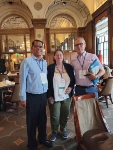 Two men and a woman, all with conference lanyards, stand together in a restaurant
