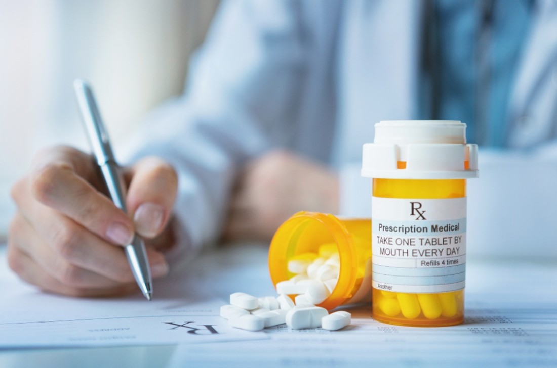 Person sits next to 2 pots of pills, one of which is spilling out onto table
