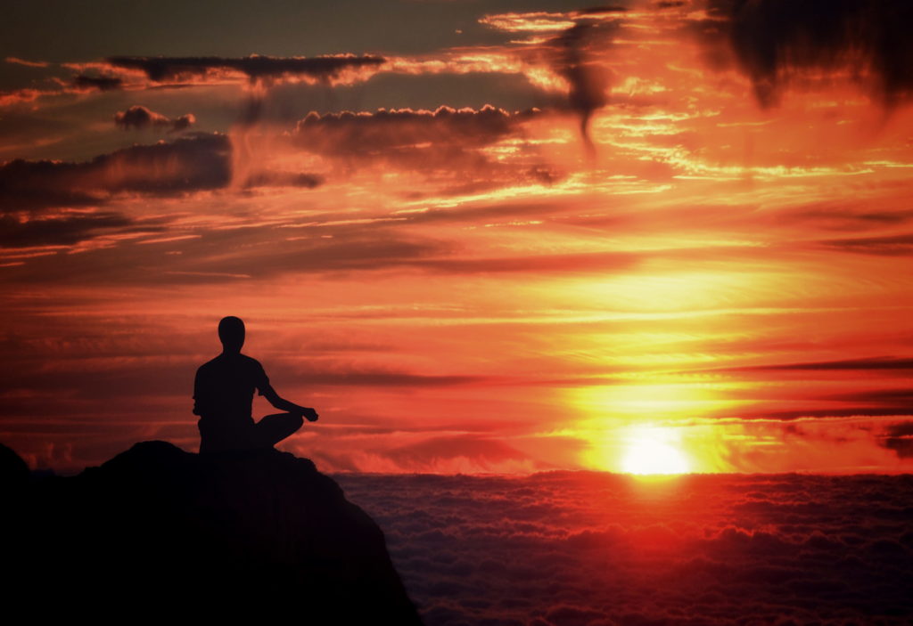 Photo of a person meditating over clouds.