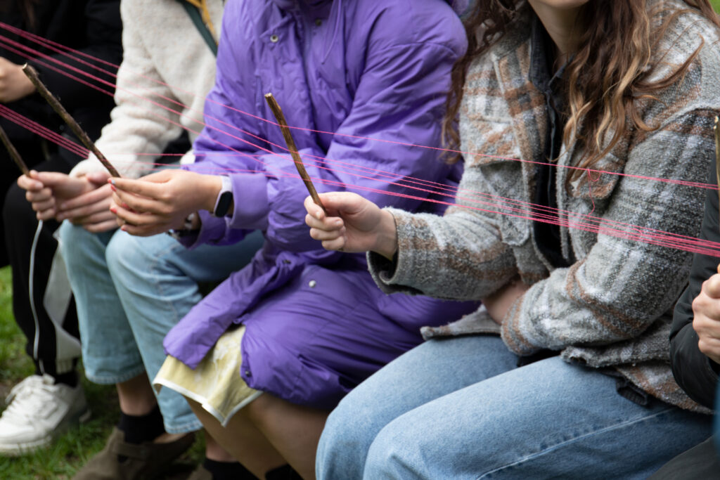 Colour photograph showing students holding wooden sticks to aid artist Antonio Pichilla in demonstrating pattern design.
