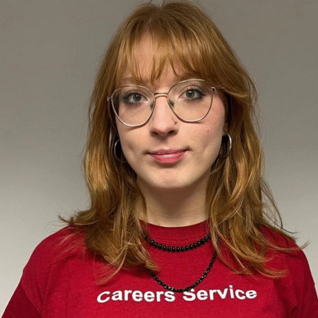Headshot of a woman with red hair wearing glasses and a red t-shirt that reads Careers Service