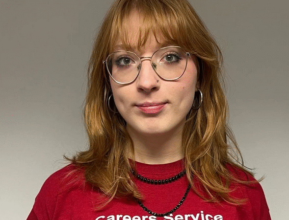 Headshot of a woman with red hair wearing glasses and a red t-shirt that reads Careers Service