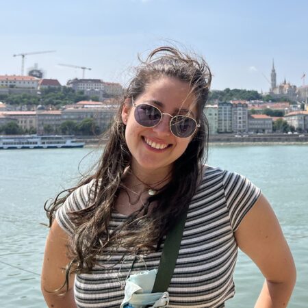 Photograph of Elisa stood in front of a river on a sunny day.