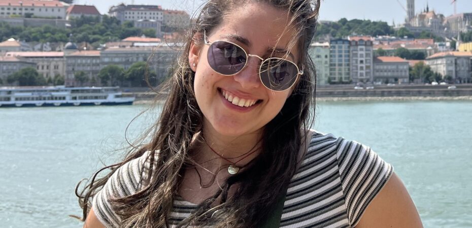 Photograph of Elisa stood in front of a river on a sunny day.