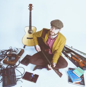 Mike Vass sits among his instruments, music books and recording equipment