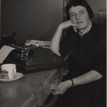 Charlotte Auerbach sits at her desk with a typewriter and cup of tea