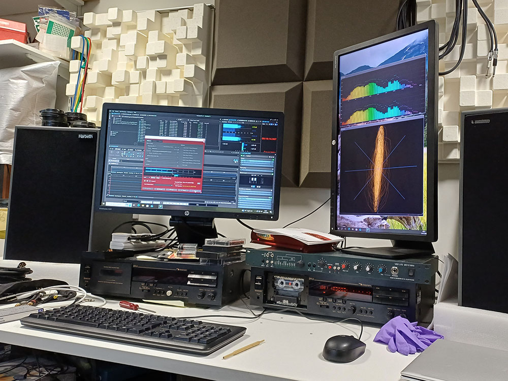 Two computer monitors sat on top of two Nakamichi cassette players, with the monitors displaying audio digitisation software. 