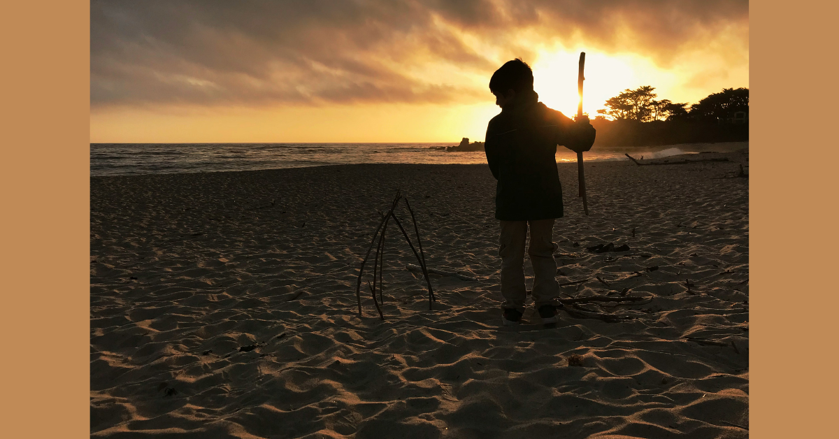 A child building a structure made from sticks on a beach