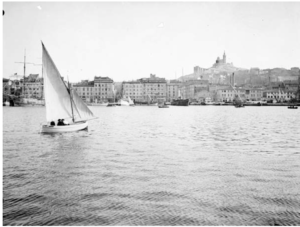 View of Quayside standing from the North bay, looking south. Beyond the water, the other side of the Quay is visible and punctuates by rows of boats and businesses. Behind them stands a hill with a Cathedral stood tall upon it.