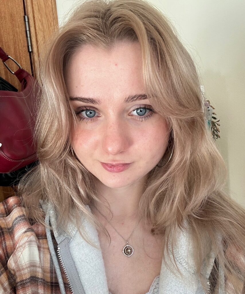 A profile image of Arianne. She is wearing a fleece and silver necklace, and smiling.