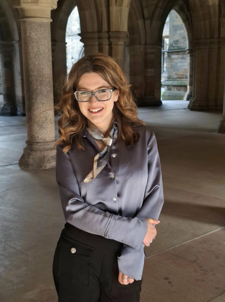 A profile image of Julia. She is standing within a stone courtyard, surrounded by pillars and archways.