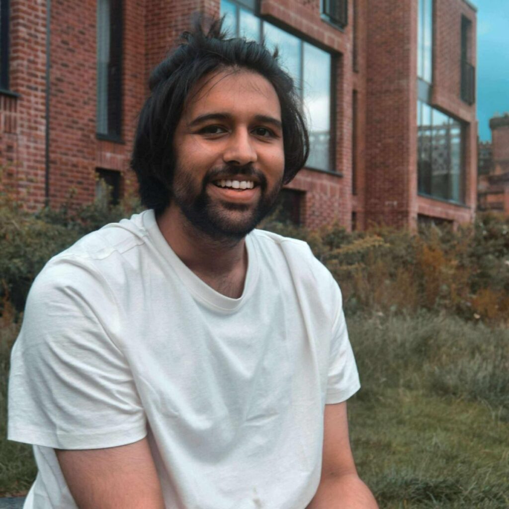 A profile image of Wurdaan. He is smiling and wearing a white t-shirt, in front of an out of focus brick building.
