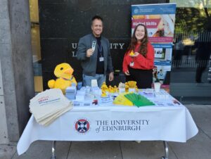Jonathan and Ricarda standing next to a stall full of merchandise outside the Main Library, George Square.