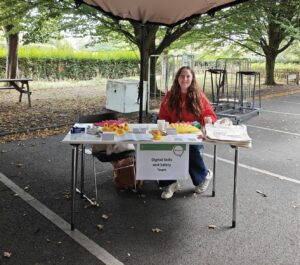 Ricarda sitting at her Digital Skills stall with lots of merchandise