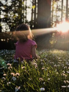 Light coming through trees on to girl sitting in a meadow of daisies