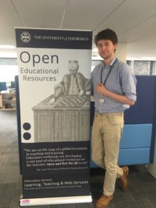 Tomas is standing next to the OER banner that contains the image of the Mechanical Turk engraving and the quote "We are on the cusp of a global revolution in teaching and learning. Educators worldwide are developing a vast pool of educational resources on the Internet, open and free for all to use" The Cape Town Open Educational Declaration 2002