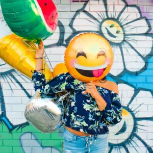 woman holding balloons in front of wall with graffiti