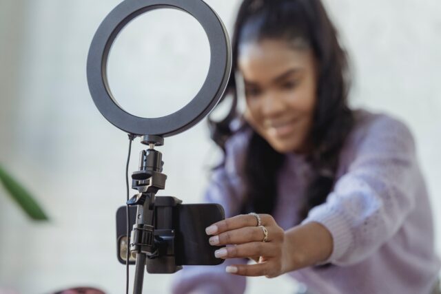 Happy young black woman setting up a camera to film using a smartphone.