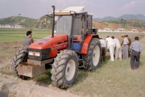 A photograph of an EU tractor, given to a potato research institute in North Korea. The tractor is in a field and is surrounded by people.
