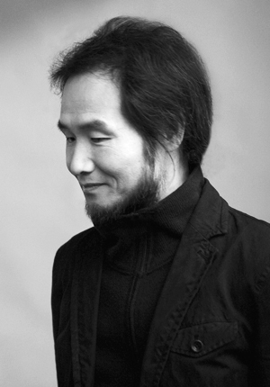 A black and white photograph of Park Nohae. He has dark hair and a beard, and is wearing black clothing.