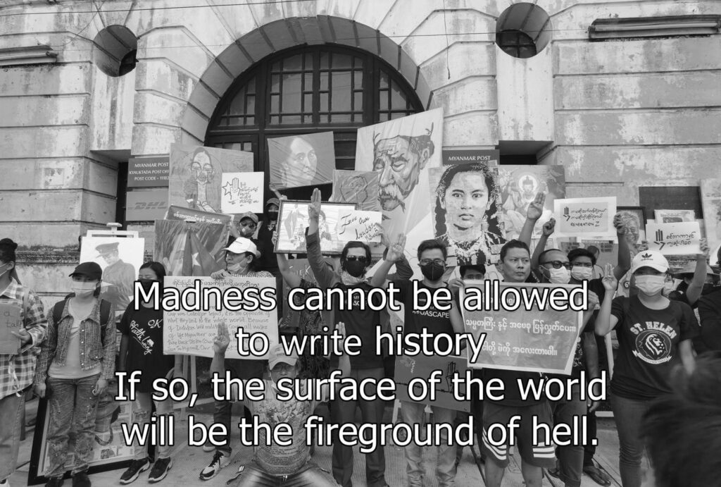 A black and white photograph of people holding signs, with the text ‘Madness cannot be allowed to write history. If so, the surface of the world will be the fireground of hell.’ superimposed at the bottom of the photo.