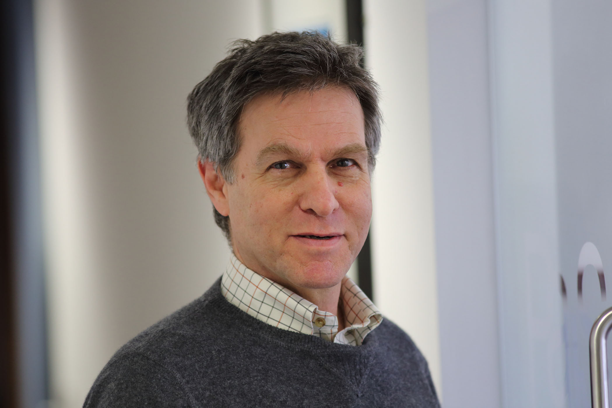 A photograph of Professor Tom Sorell, who has dark hair and is wearing a grey jumper and checked shirt.