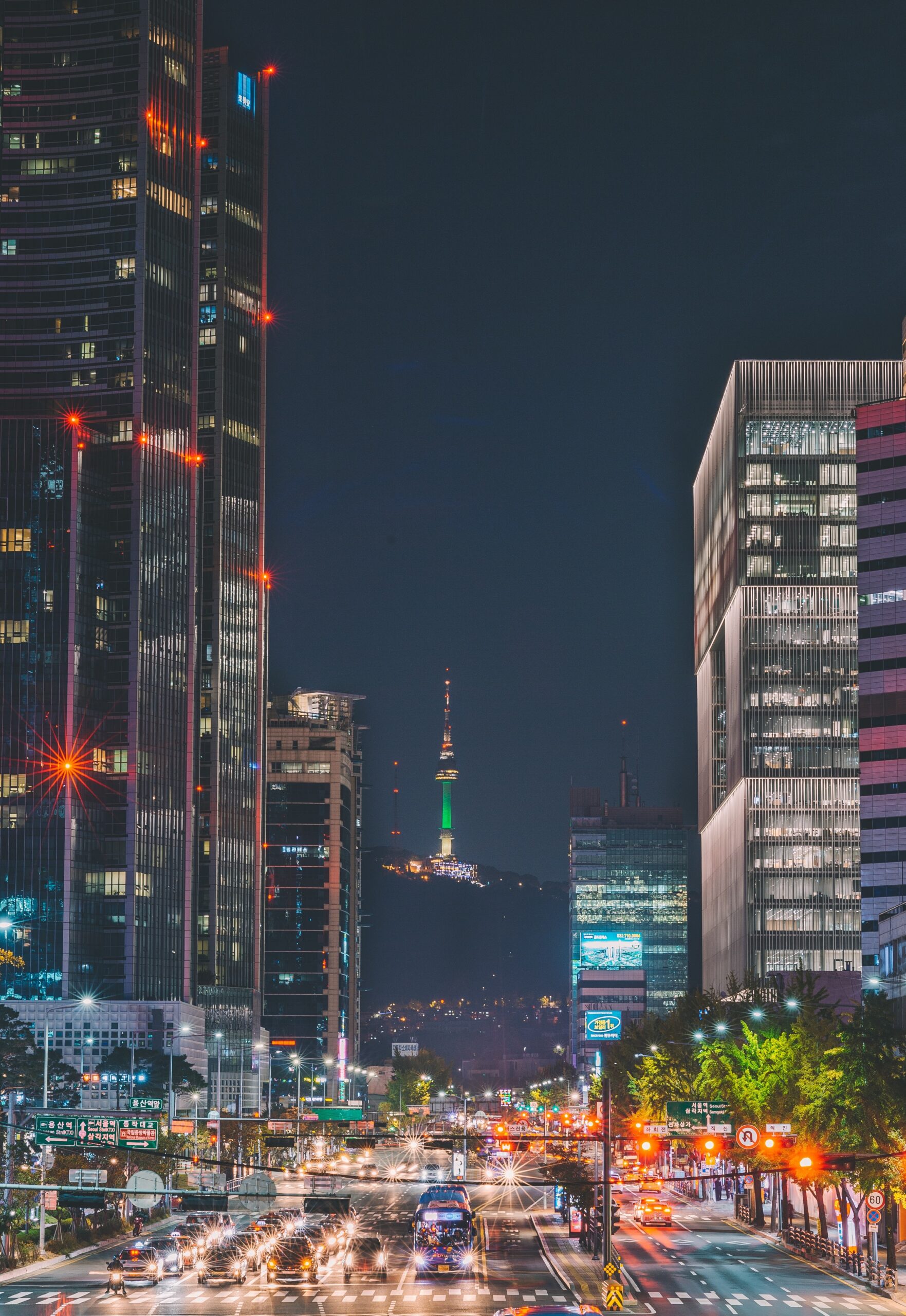 A photograph of Seoul, South Korea at night. In the foreground are cars and buildings, and in the background is Namsan and an illuminated N Seoul Tower.