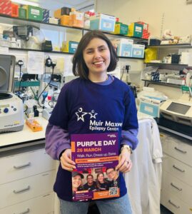 portrait of jessica mahon in a lab with purple day promo materials and muir maxwell tshirt