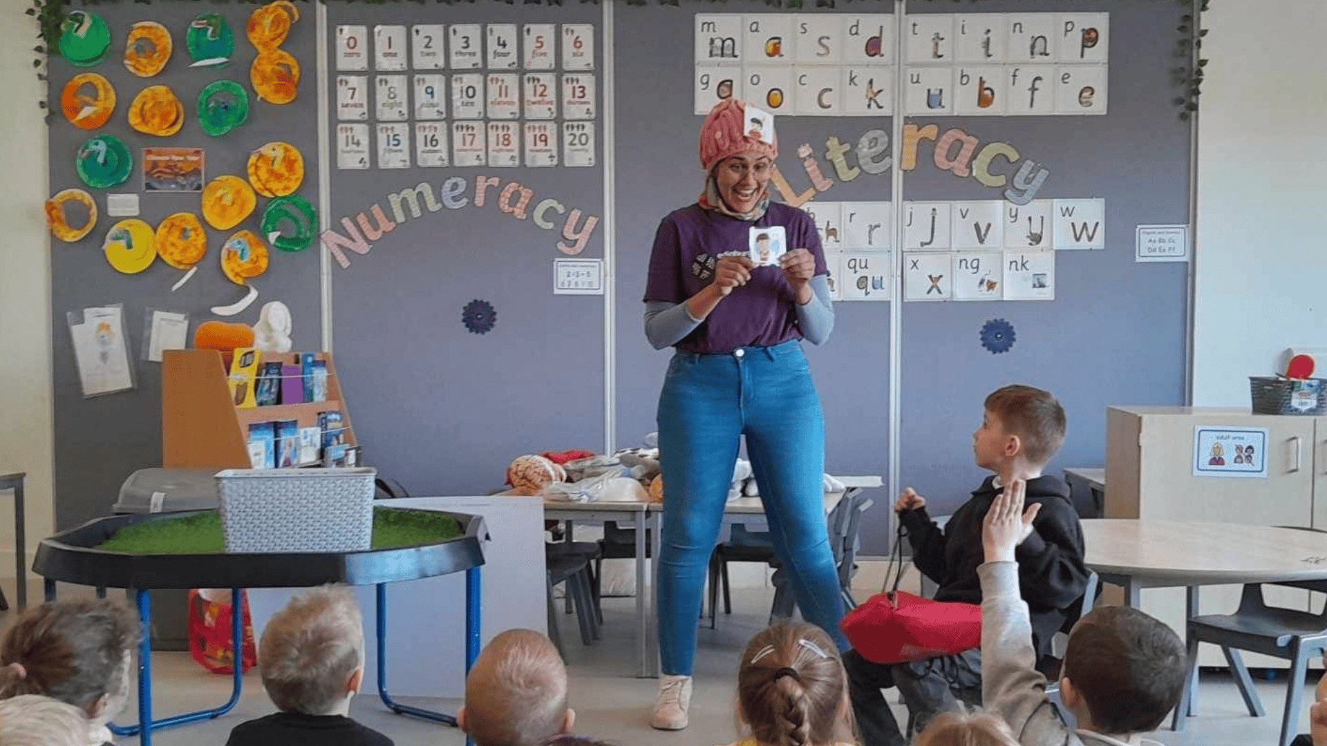 presenter in classroom holding up a card. Children sitting listening