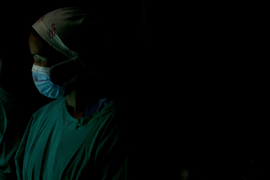 Dark background with doctor in scrubs, hat and mask