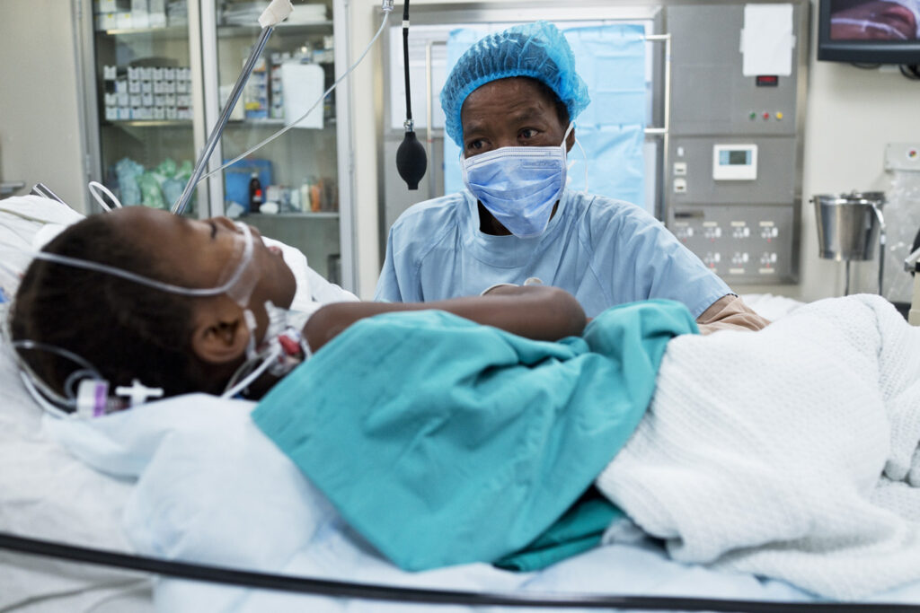 Patient in recovery area following surgery which medical professional looks on.