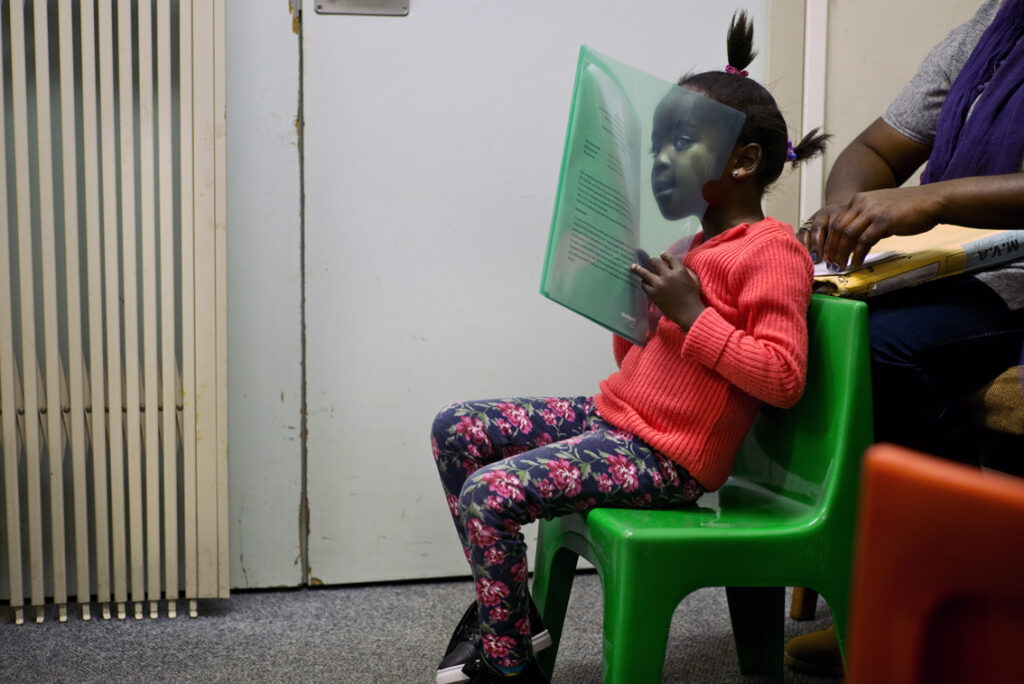 Young patient sitting on a green chair holding a green folder in her hands.