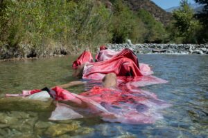 Landscape photograph of bodies bathing in an outdoor body of water and draped in red cloth
