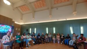 Photograph of people sitting in a large circle in a room.