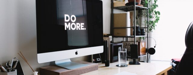 Apple desktop computre on a wooden desk with shelves to the side. "Do More" in white lettering on a black screen.