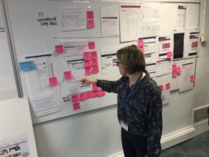 Woman presents at whiteboard covered in screenshots and post it notes