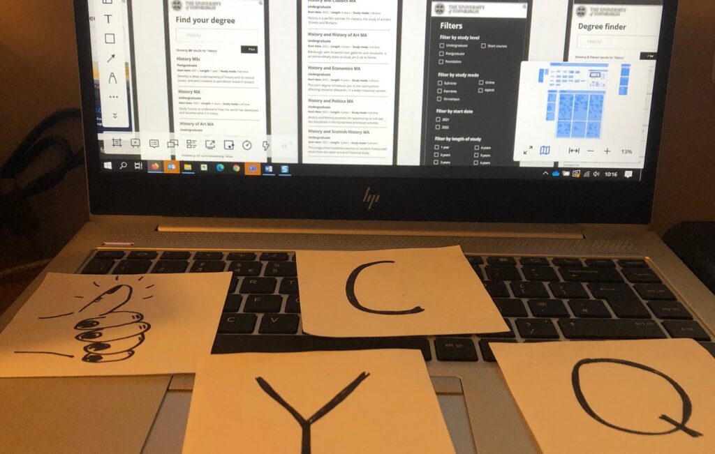 Four squares of paper on a laptop keyboard. They read: Y, C, Q and a sketch of a raised thumb