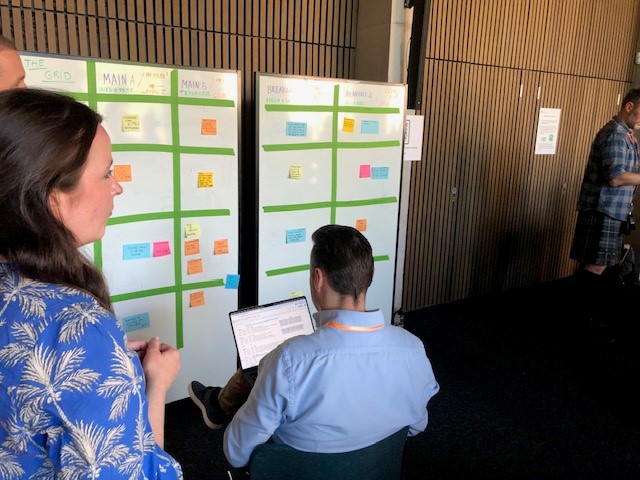 Man sits at laptop looking at a board of post-it notes