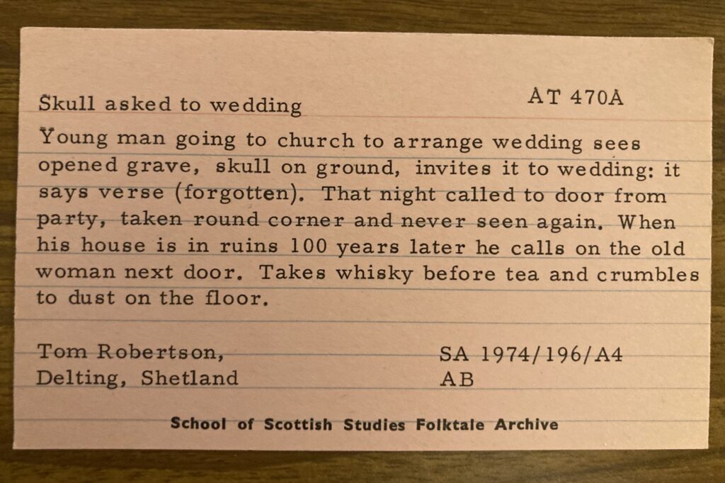The card reads " Skull asked to wedding. Young man going to church to arrange wedding sees opened grave, skull on ground, invites it to wedding; it says a verse. That night called to door from party, taken around corner and never seen again. When his house is in ruins 100 years later he calls on the old woman next door. Takes whisky before tea and crumbles to dust on the floor"