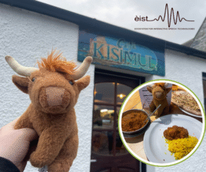 Image Description: The main photo features a small, stuffed plush toy of a Highland Cow with horns infront of a white building that has a colourful sign that says ‘Café Kisimul’. There is a second, smaller circular image in the bottom right-hand corner of an Indian meal with naan bread, curry and yellow rice on a table. It is taken inside the location of the main photo. There is a plate with a serving of rice and curry, a dish of curry with a spoon, and a large piece of naan on another plate. A plush toy resembling a brown Highland cow with horns is sitting near the food with a menu behind them.