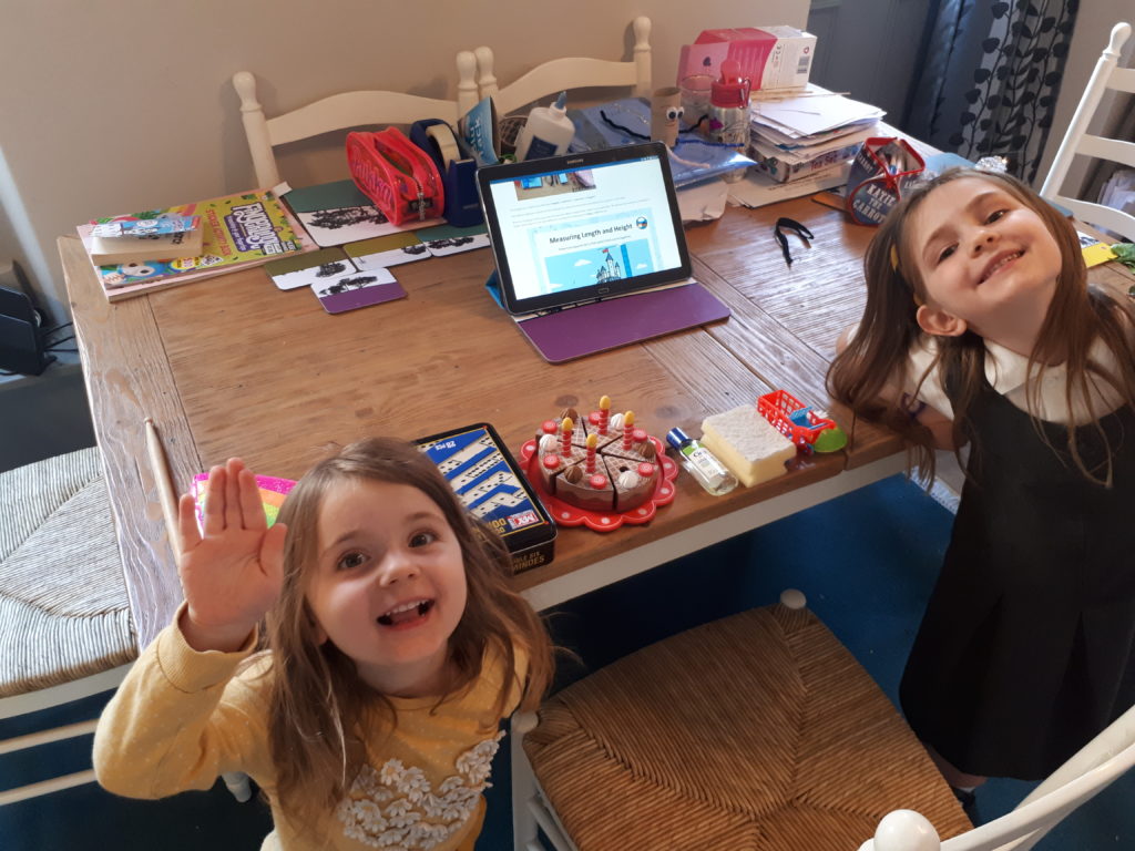 two children at a table waving to the camera behind them