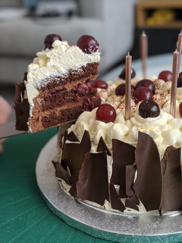 Cream covered cake layered with chocolate and cherries. Cake slice pull out a piece showing two layered sponges of chocolate cake.