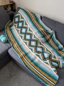 Yellow blue and white knitted blanket laid out across a sofa