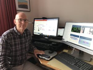David Porteous sat at his desk with monitors displaying the Generation Scotland website