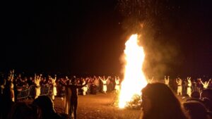 Many figures standing round a Beltane bonfire.